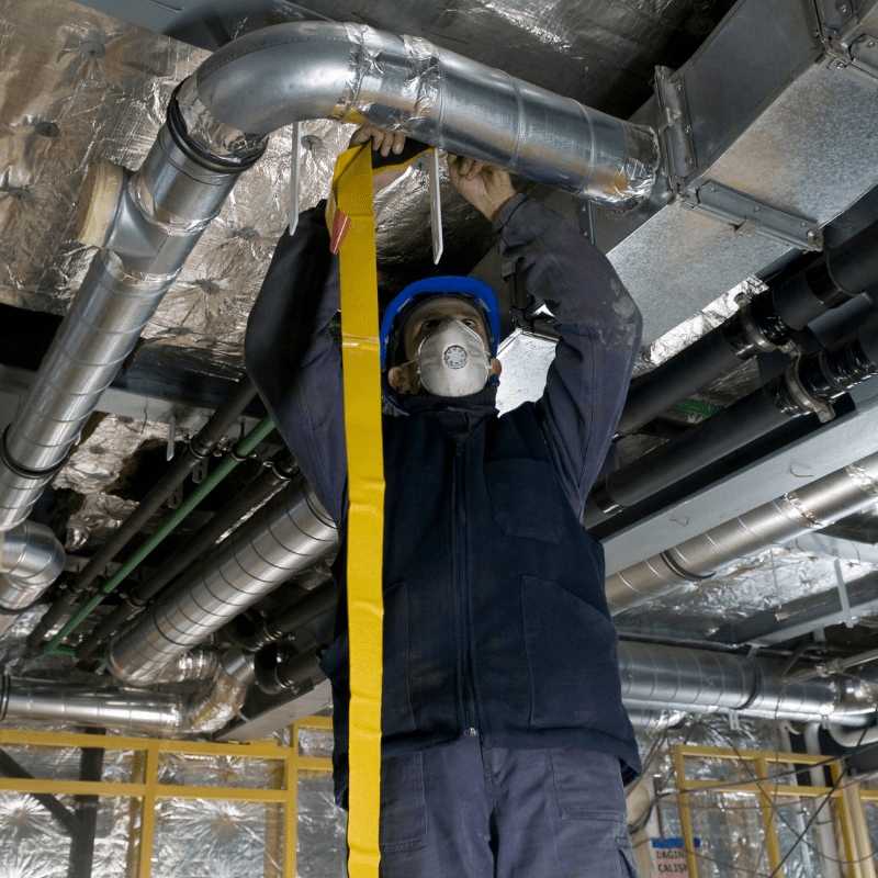 HVAC technician sealing commercial air ducts in building ceiling